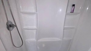 A shower with a handheld showerhead and a small shelf with a bottle.