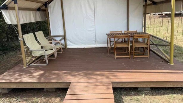 A tent with a wooden deck, two lounge chairs, and a table.