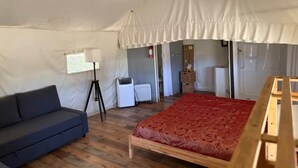 A tented room with a bed, a sofa, a lamp, and a heater.