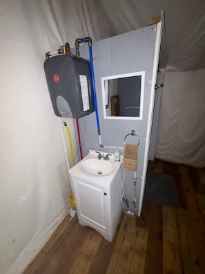 Un baño pequeño con lavamanos blanco, espejo y calentador de agua.