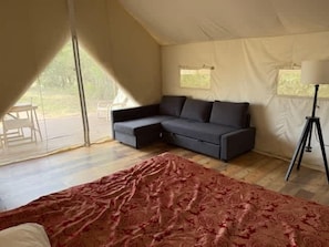 A tented accommodation with a sofa, a bed, and a tripod lamp. - Serenity Tent Number 2 (Denison)
