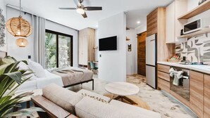 A modern hotel room with a sofa, a small round table, a ceiling fan, and a kitchen area with a microwave. - Northside Retreat - Infinity pool - Fast Wi-Fi (Sayulita)