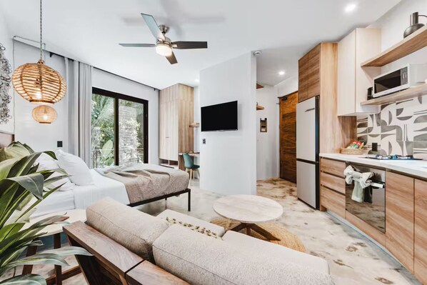 A modern hotel room with a sofa, a small round table, a ceiling fan, and a kitchen area with a microwave. - Northside Retreat - Infinity pool - Fast Wi-Fi (Sayulita)