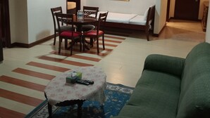 Habitación de hotel con zona de comedor, sofá, una mesita con un mando a distancia y una cama.