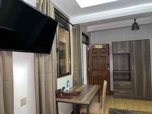 A room with a TV mounted on the wall, a wooden desk with a chair, a wardrobe, and a door labeled '502'.