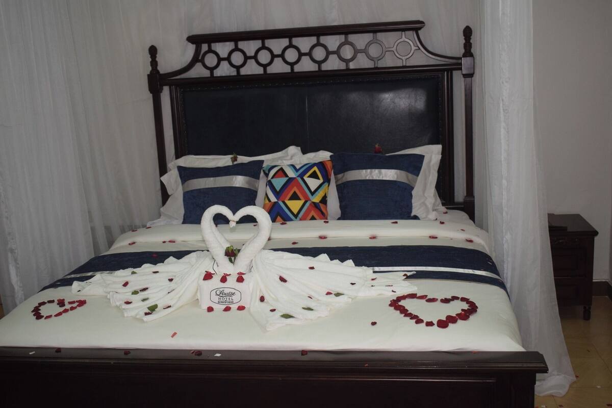 A bed with a heart-shaped arrangement of rose petals and a swan-shaped towel arrangement.