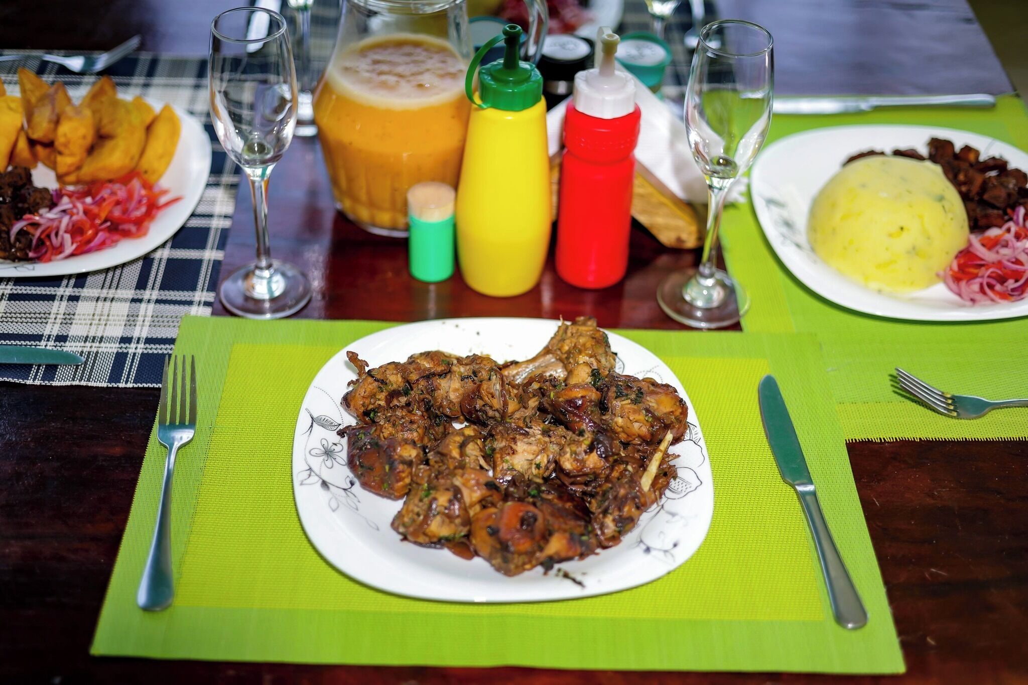 Una mesa de comedor servida con platos de comida, salsas y vasos.