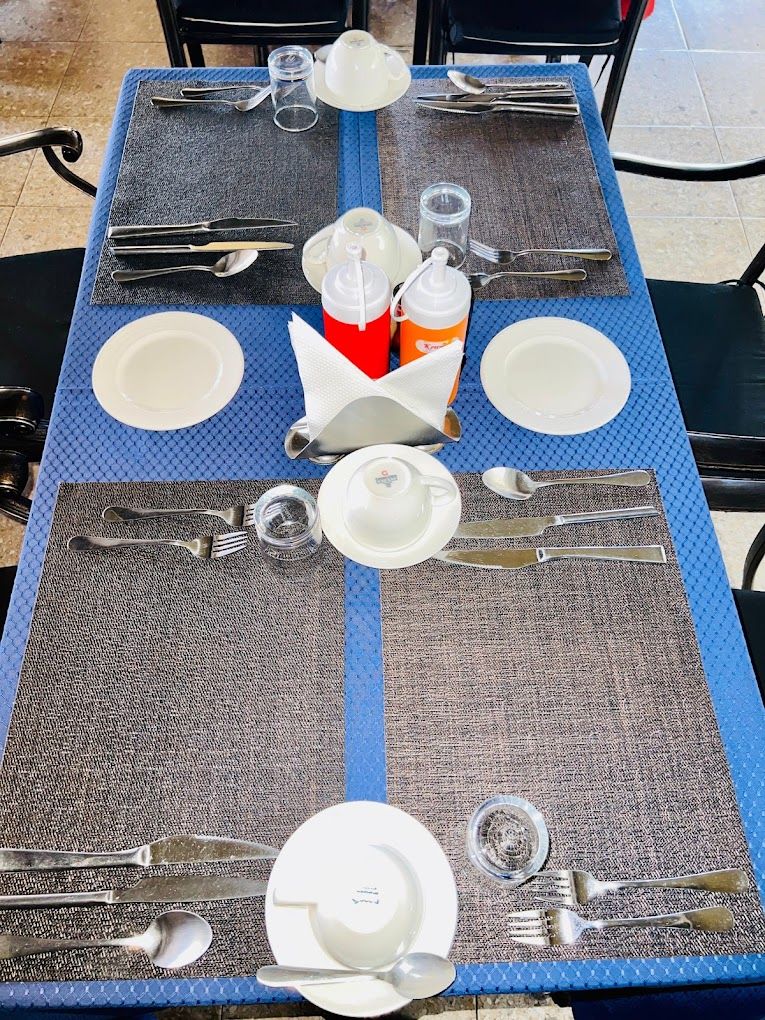 A table set for four with placemats, plates, cutlery, and condiment bottles.