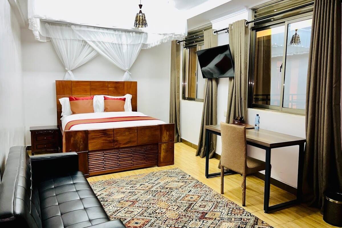A bedroom with a wooden bed, a desk, a chair, a TV, and a patterned rug.