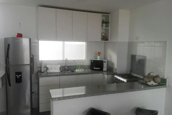 A modern kitchen with white cabinets, a stainless steel refrigerator, a microwave, and a sink.