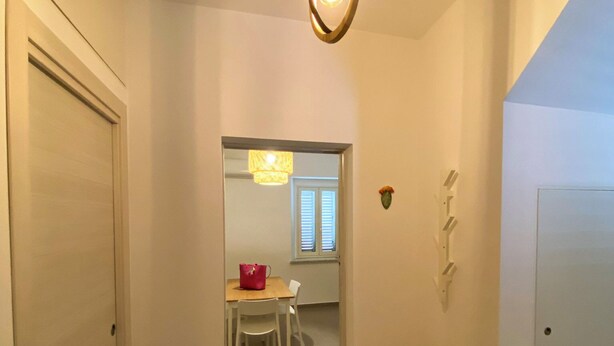 A hallway with a wooden door, a small table with a red bag, and a hanging light fixture. - La Casetta (Stalettì)
