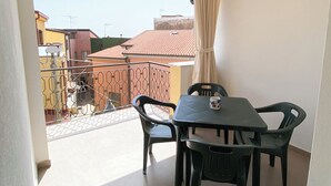 A balcony with a dining table and chairs, a view of neighboring buildings, and a curtain on the window. - La Casetta (Stalettì)
