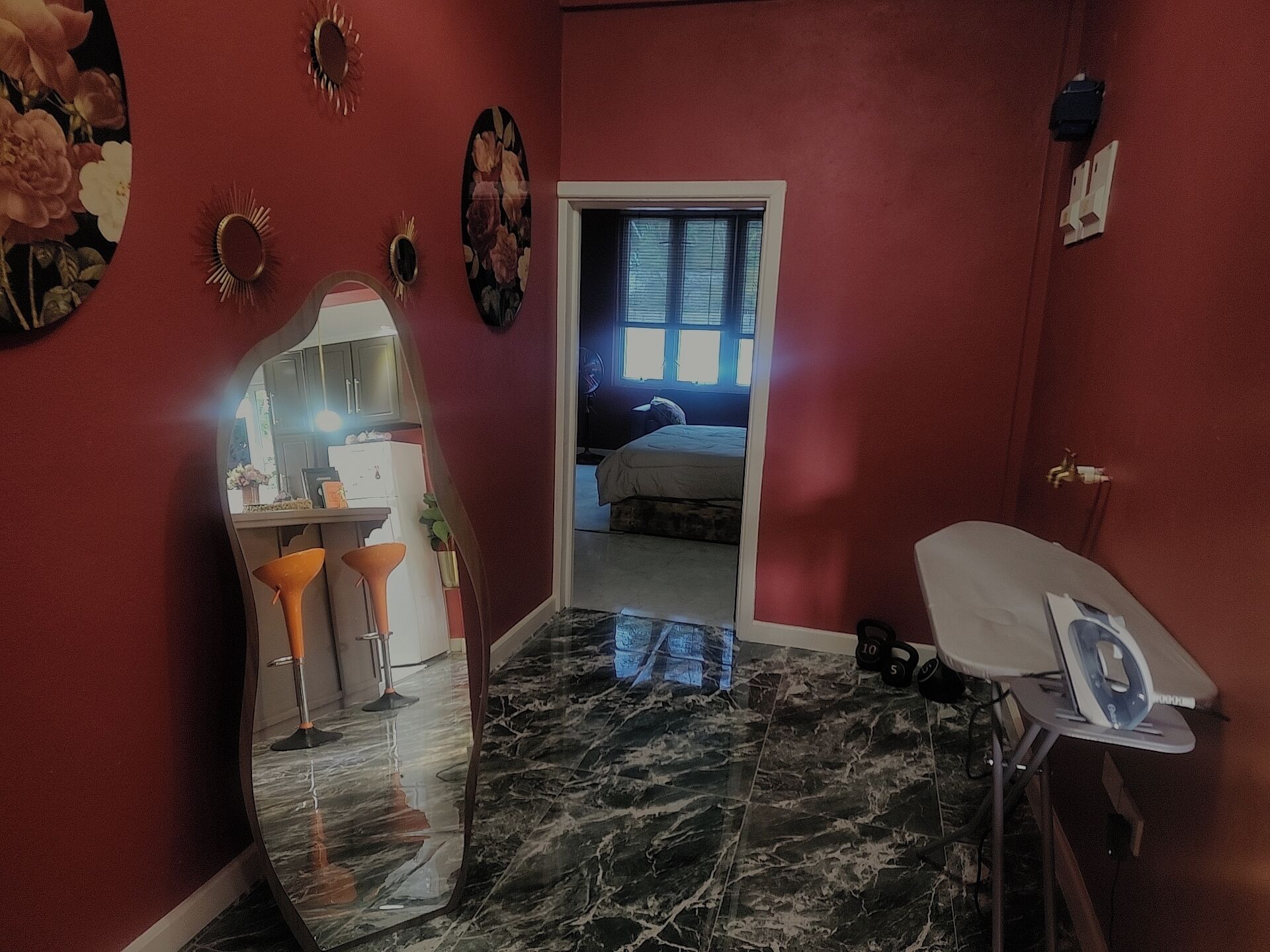 A compact room with a marble floor, a bed, a desk with a chair, a mirror, and a small ironing board.