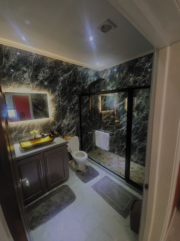 A modern bathroom with a marble backsplash, a glass-enclosed shower, and a vanity with a sink and mirror.