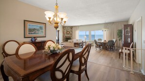 Ein Essbereich mit Holztisch und Stühlen, einer Chandelierleuchtre und Blick auf das Meer durch große Fenster.