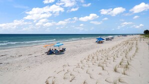 Ein Strand mit Reihen von Liegestühlen und Sonnenschirmen, ein sandiger Uferstreifen und das Meer im Hintergrund.