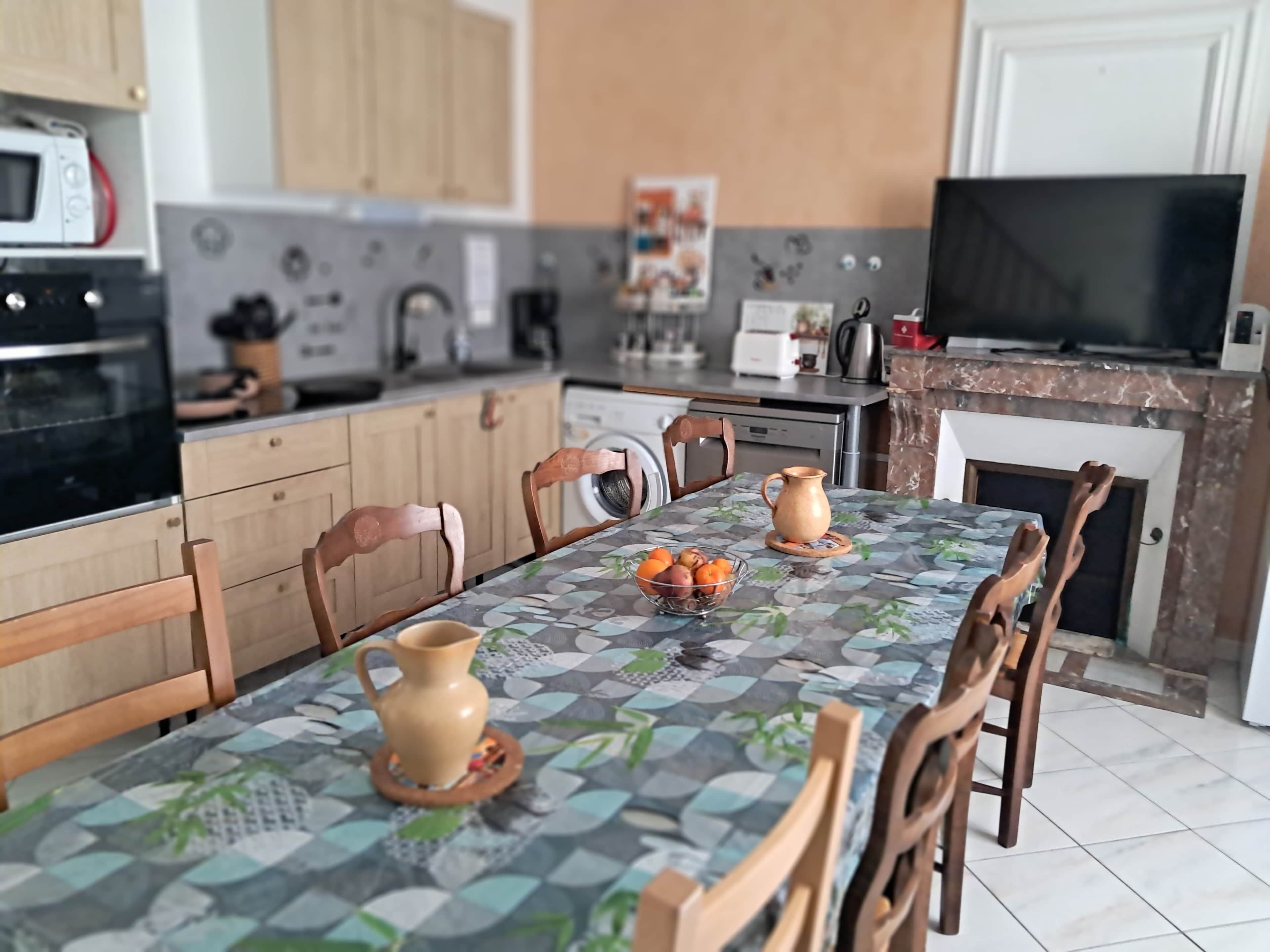 Una cocina moderna con armarios de madera, una mesa de comedor con mantel estampado y un televisor.