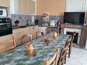 A modern kitchen with wooden cabinets, a dining table with a patterned tablecloth, and a television.