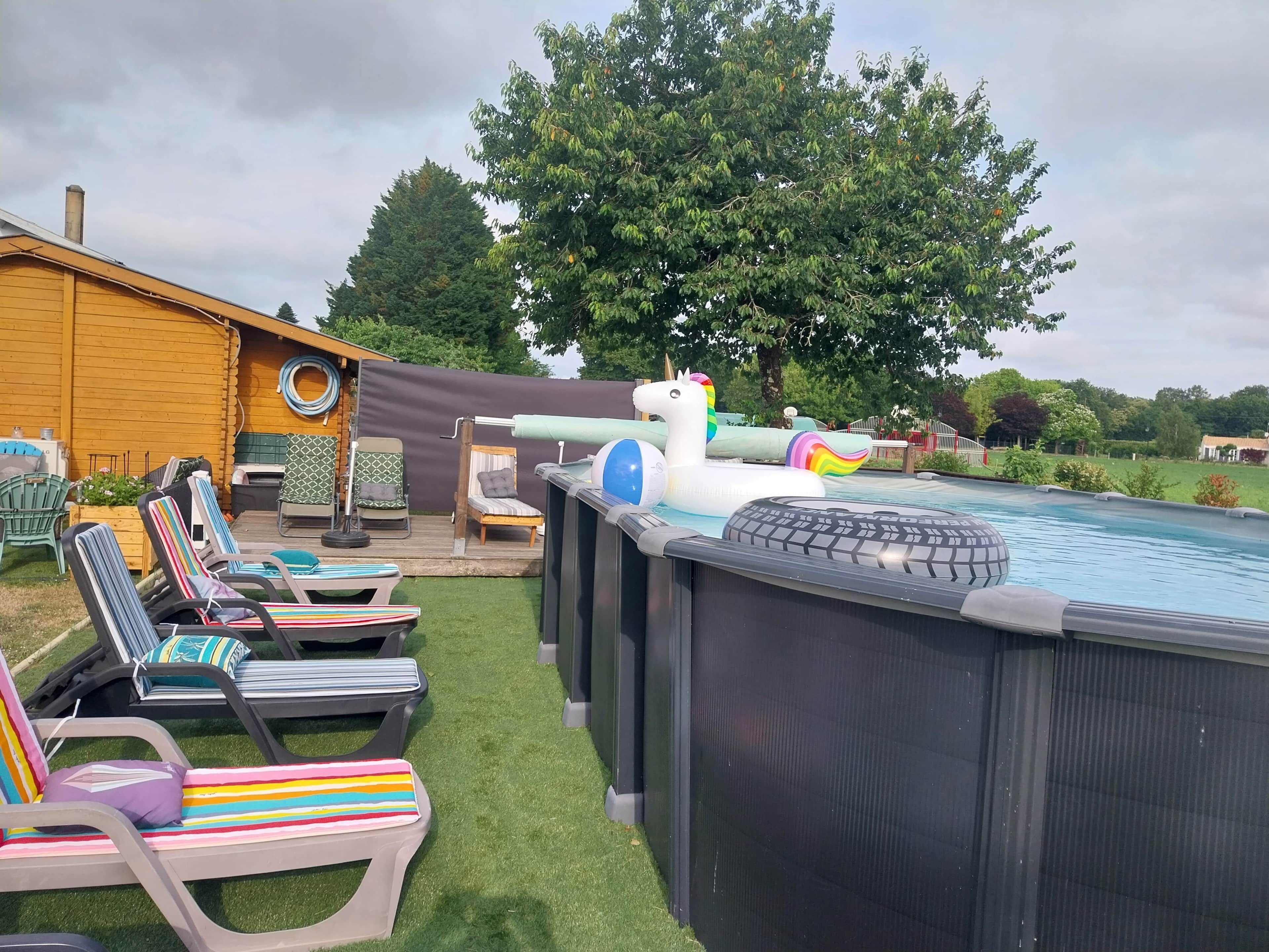 An outdoor swimming pool area with inflatable toys, lounge chairs, and a wooden deck.