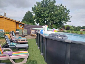An outdoor swimming pool area with inflatable toys, lounge chairs, and a wooden deck.