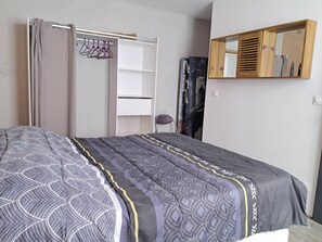 A bedroom with a bed, a wardrobe, a mirror, and a wall-mounted shelf.
