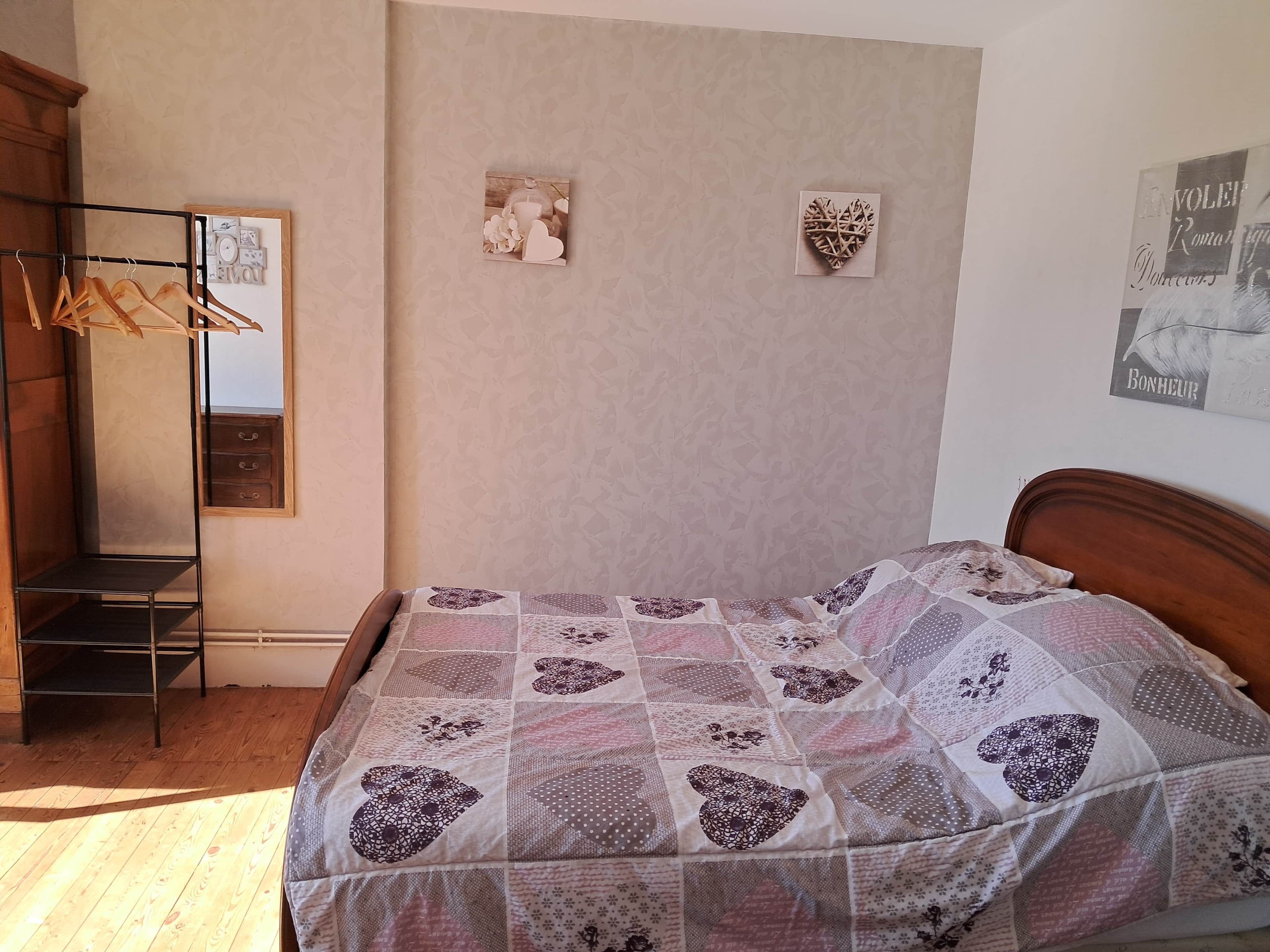 A bedroom with a wooden bed, a hanging clothes rack, a mirror, and two wall decorations.