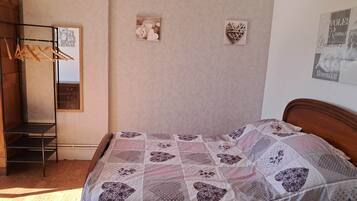 A bedroom with a wooden bed, a hanging clothes rack, a mirror, and two wall decorations.