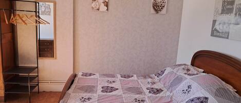 A bedroom with a wooden bed, a hanging clothes rack, a mirror, and two wall decorations.