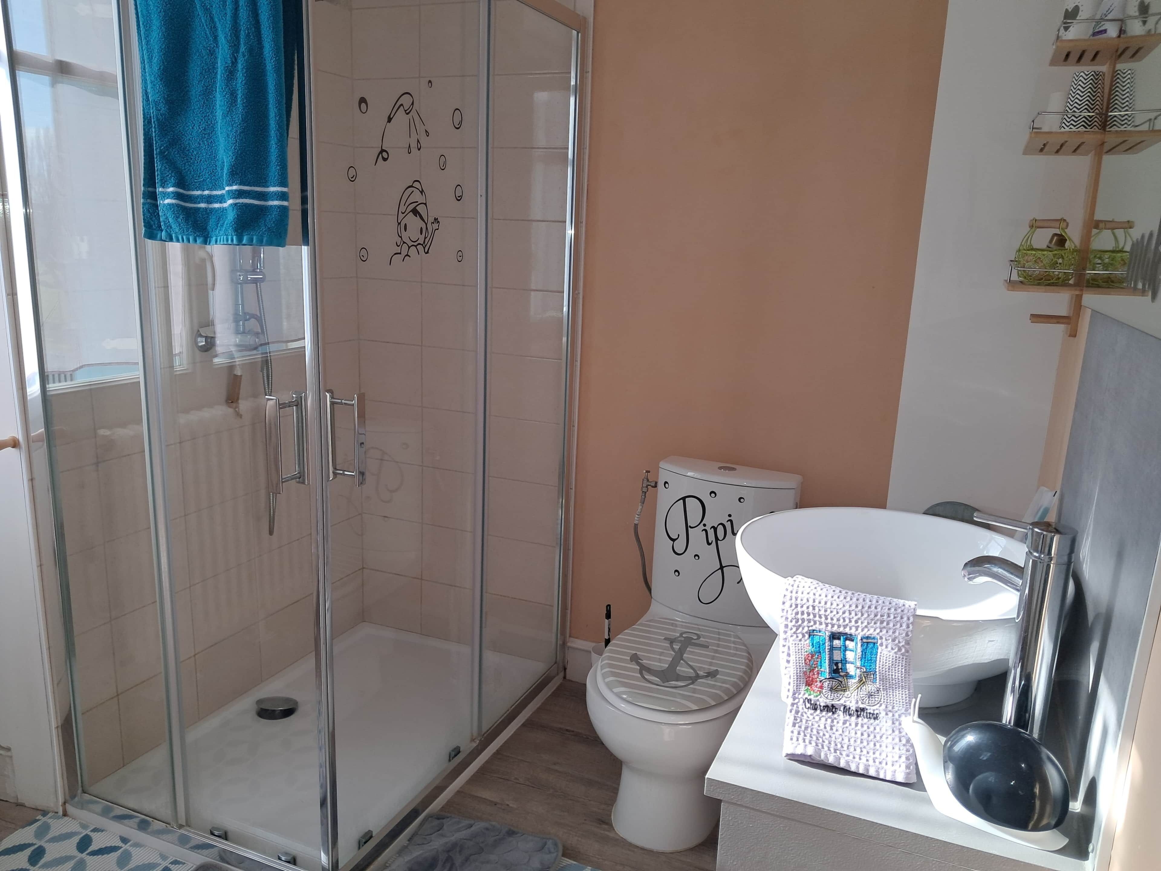 Ein Badezimmer mit einer Duschkabine, einer Toilette mit dekorativem Deckel und einem Waschbecken mit Handtuchhalter.