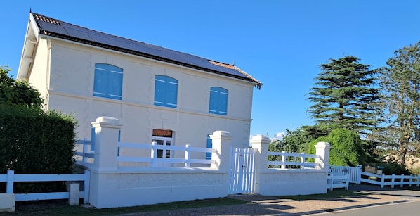 Un bâtiment à deux étages, doté d’une façade blanche, d’une entrée fermée par un portail et surplombé d’un ciel d’un bleu éclatant.