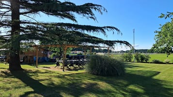A well-maintained garden with a wooden pergola, outdoor seating, and a large tree providing shade.