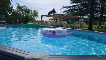 Une piscine avec des jeux gonflables, entourée d’arbres et agrémentée d’une pergola en bois.