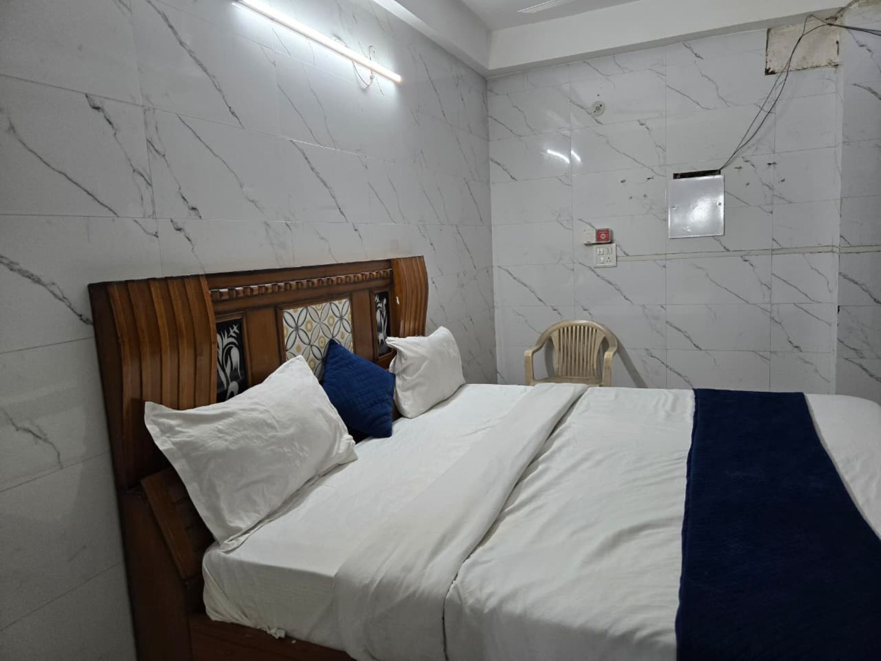 Een netjes opgemaakt bed met witte en blauwe kussens, een houten hoofdbord en een blauwe plaid.