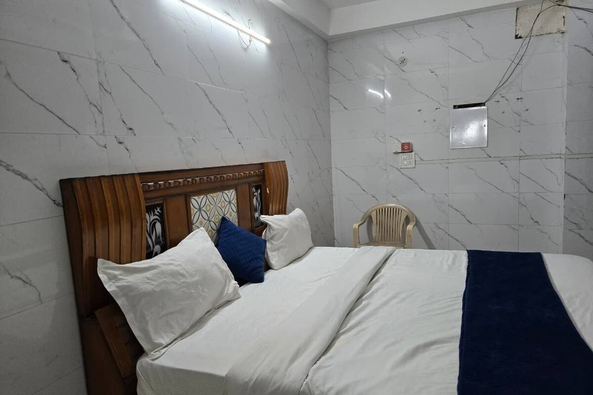 A hotel room with a marble wall, a wooden headboard, a bed with white and blue bedding, and a chair.