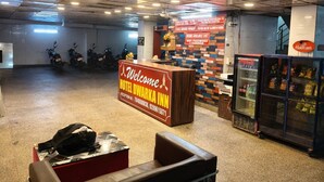 Zona reception di un hotel con un cartello 'Welcome', una scrivania della reception, una parete con un motivo colorato, un frigorifero fornito di bevande e motociclette parcheggiate sullo sfondo.