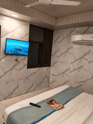 Ein Hotelzimmer mit einem Bett, einem an der Wand montierten Fernseher, einem Fenster und einer Klimaanlage.