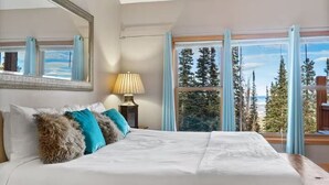 A bedroom with a large bed, a bedside lamp, a mirror, and a window with a view of trees and a clear sky. - The Summit at 11 • 15 Min to Breck • Private Hot Tub Views •  Sauna •... (Breckenridge)