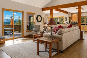 A spacious living room with a sofa, a coffee table, and a chair. There is a dining table with chairs and a view of the mountains through the glass doors. - Hot Tub· Game Room· Sauna· Mtn Views· Dog Friendly (Breckenridge)