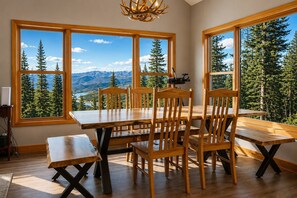 A dining area with a table and chairs, large windows with a mountain view, and a chandelier. - Hot Tub· Game Room· Sauna· Mtn Views· Dog Friendly (Breckenridge)
