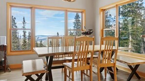 A dining area with a large table and chairs, large windows with a view of trees and mountains, and a chandelier. - The Summit at 11 • 15 Min to Breck • Private Hot Tub Views •  Sauna •... (Breckenridge)