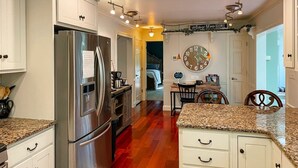 Una cocina con gabinetes blancos, electrodomésticos de acero inoxidable, encimeras de granito y un comedor con un reloj en la pared.