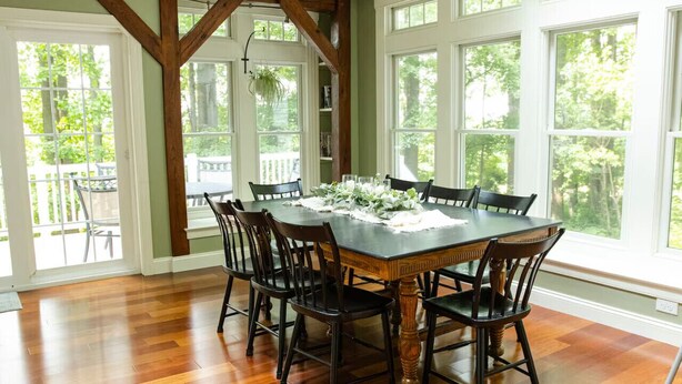 Comedor con una gran mesa de madera rodeada de sillas, ventanas amplias y vista a la vegetación exterior.