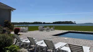 A pool area with white chairs and tables, a clear sky, and a view of a lake. - Sunset Shores | an ESVR property (Royal Oak)