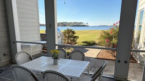 A covered patio with a table and chairs, overlooking a body of water and a grassy area. - Sunset Shores | an ESVR property (Royal Oak)