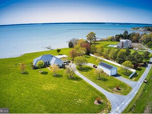 An aerial view of a residential area with a large house, a smaller house, and a dock extending into a lake. - Sunset Shores | an ESVR property (Royal Oak)