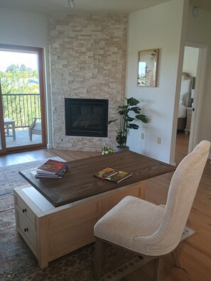 Ein Wohnzimmer mit einem an einer Ziegelwand montierten Fernseher, einem Couchtisch mit Büchern, einem weißen Sessel und einem Balkon mit Blick.