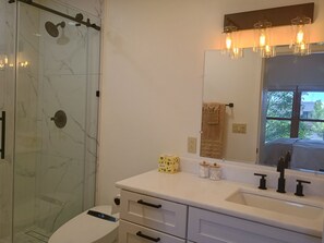 Un bagno con cabina doccia in vetro, un lavandino bianco con specchio e un portascopevoli.