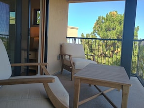 Ein Balkon mit Holztisch und zwei Stühlen, einer Glastür und Blick auf Bäume.