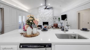 A modern kitchen with a central island, built-in stone wall, and a ceiling fan. - Backyard Oasis: Pool, Hot Tub, Giant Chess & Golf (Fort Worth)