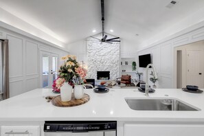 A modern kitchen with a central island, built-in stone wall, and a ceiling fan. - Backyard Oasis: Pool, Hot Tub, Giant Chess & Golf (Fort Worth)